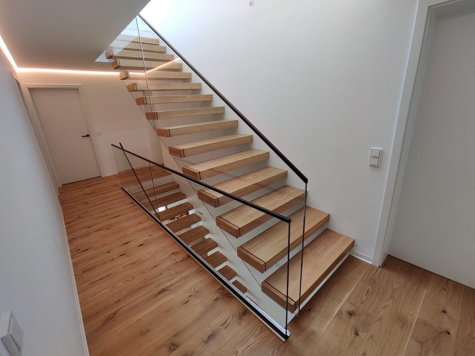 Kragarmtreppe in Eiche mit Ganzglasgeländer und schwarzem Handlauf, Blick von oben über den Lauf – AN Treppenbau
