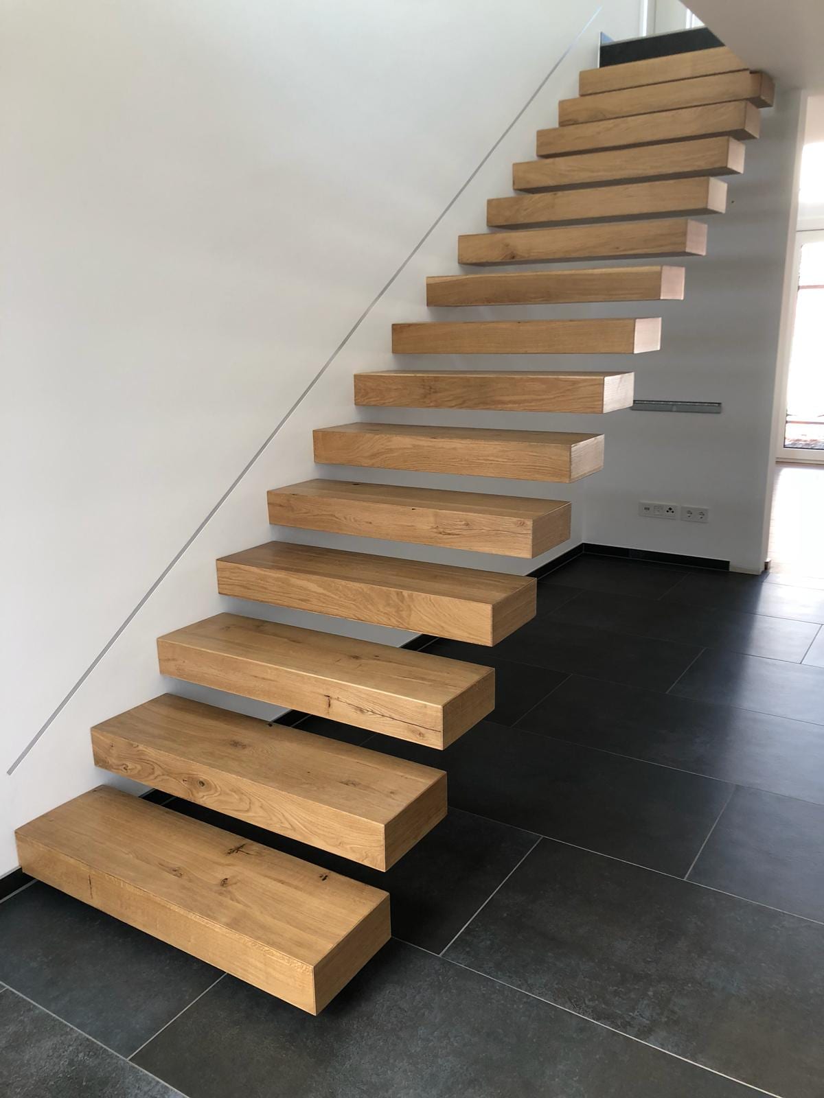 Kragarmtreppe Eiche mit Glasgeländer über dunklem Fliesenboden – AN Treppenbau