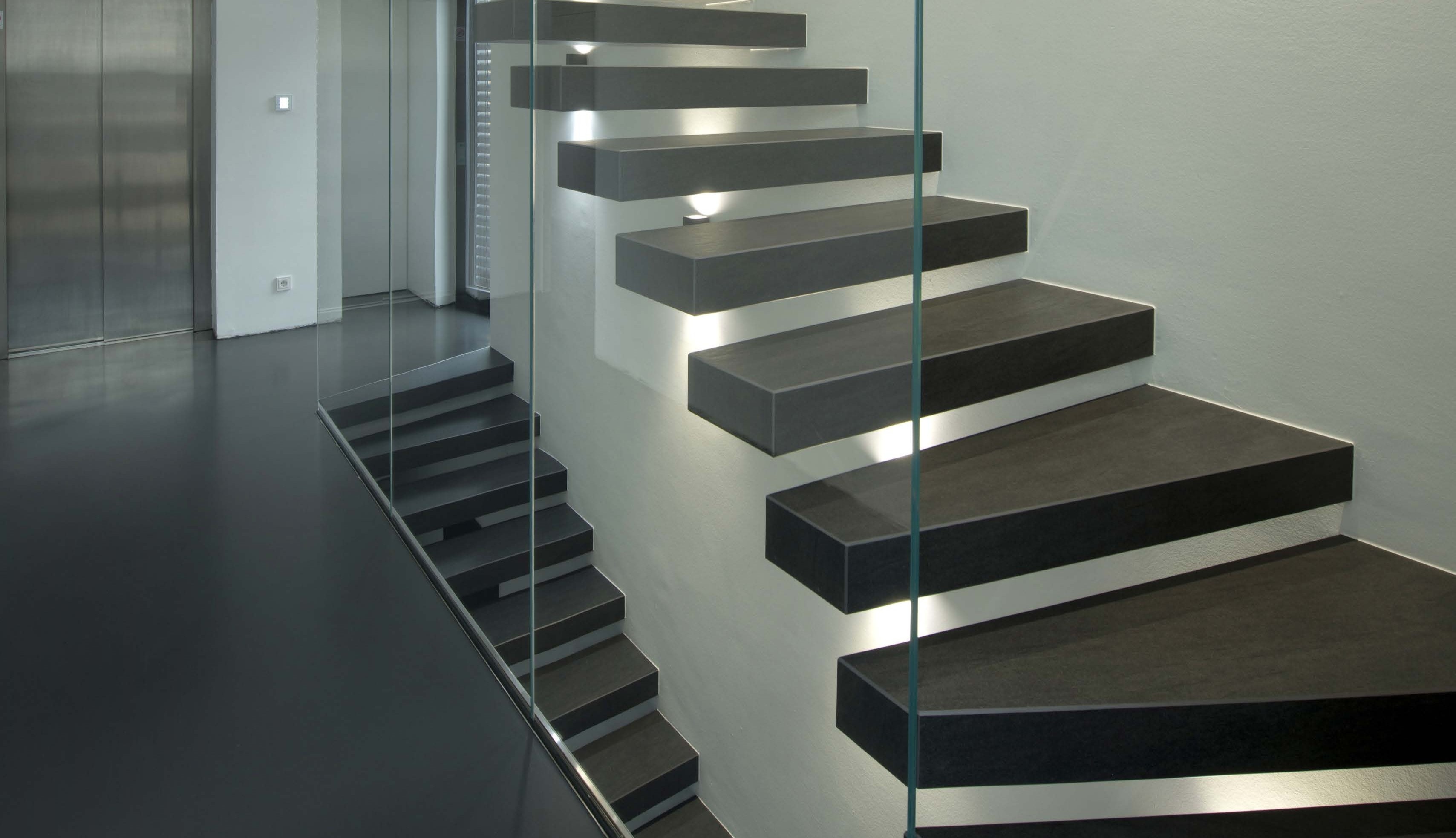 Kragarmtreppe mit dunkelgrauen Stufen in Betonoptik, Wandspots unter den Stufen – AN Treppenbau