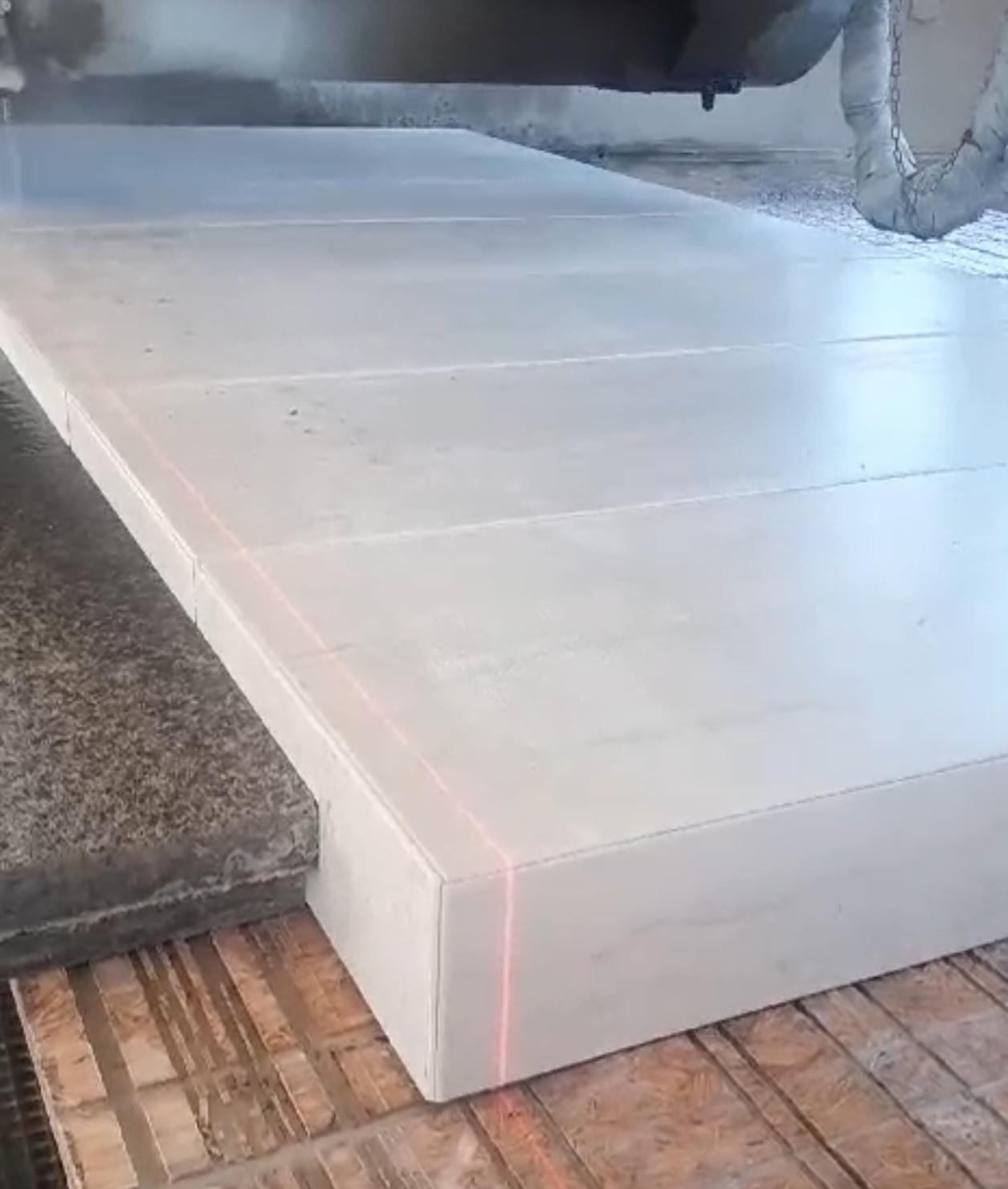 Helle Platte mit dicker Vorderkante auf dem Maschinentisch, roter Laserstrich über Fläche und Kante – AN Treppenbau