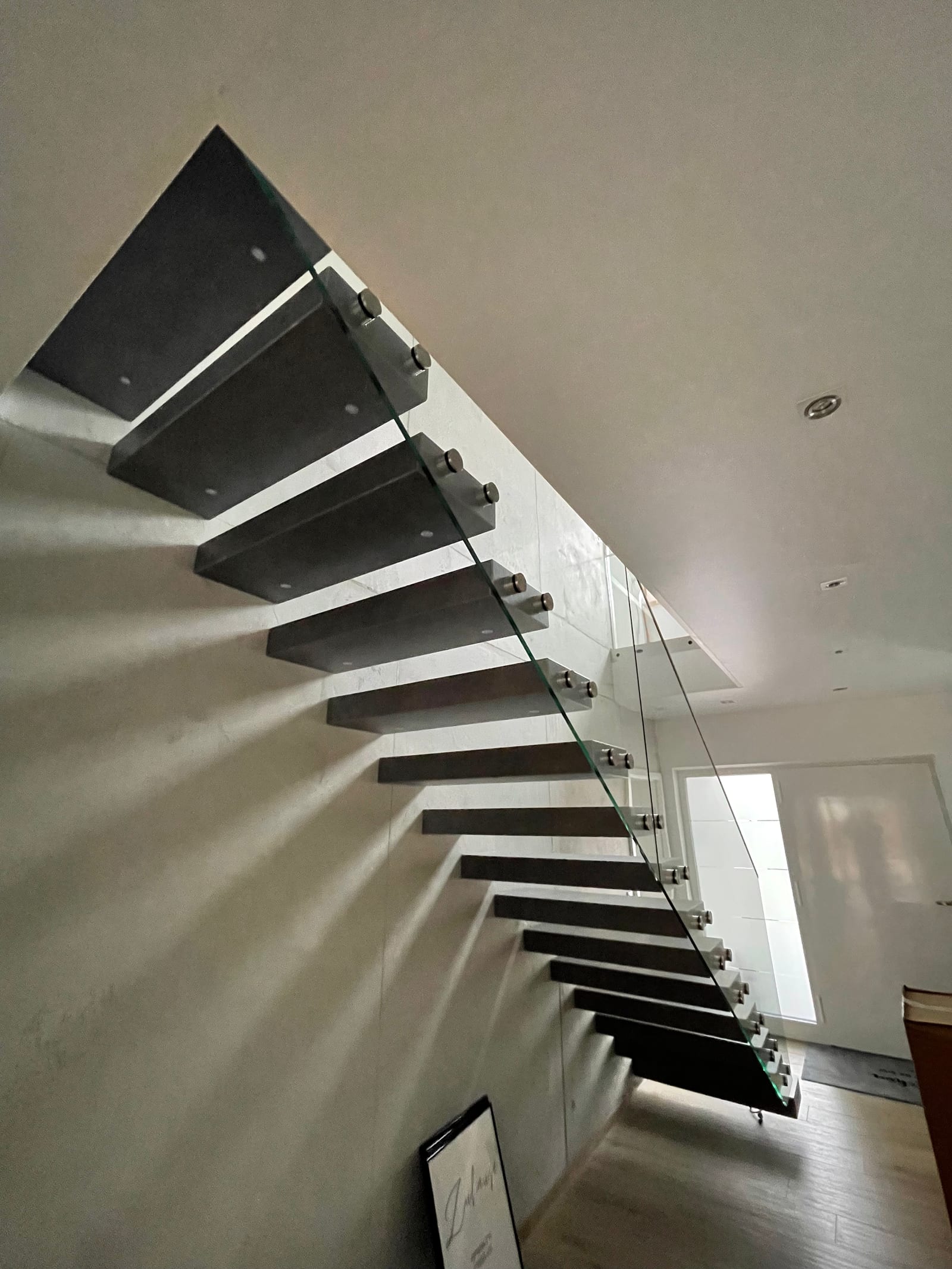 Kragarmtreppe mit dunklen, kastenförmigen Stufen von unten fotografiert, Glasgeländer mit Punkthaltern – AN Treppenbau