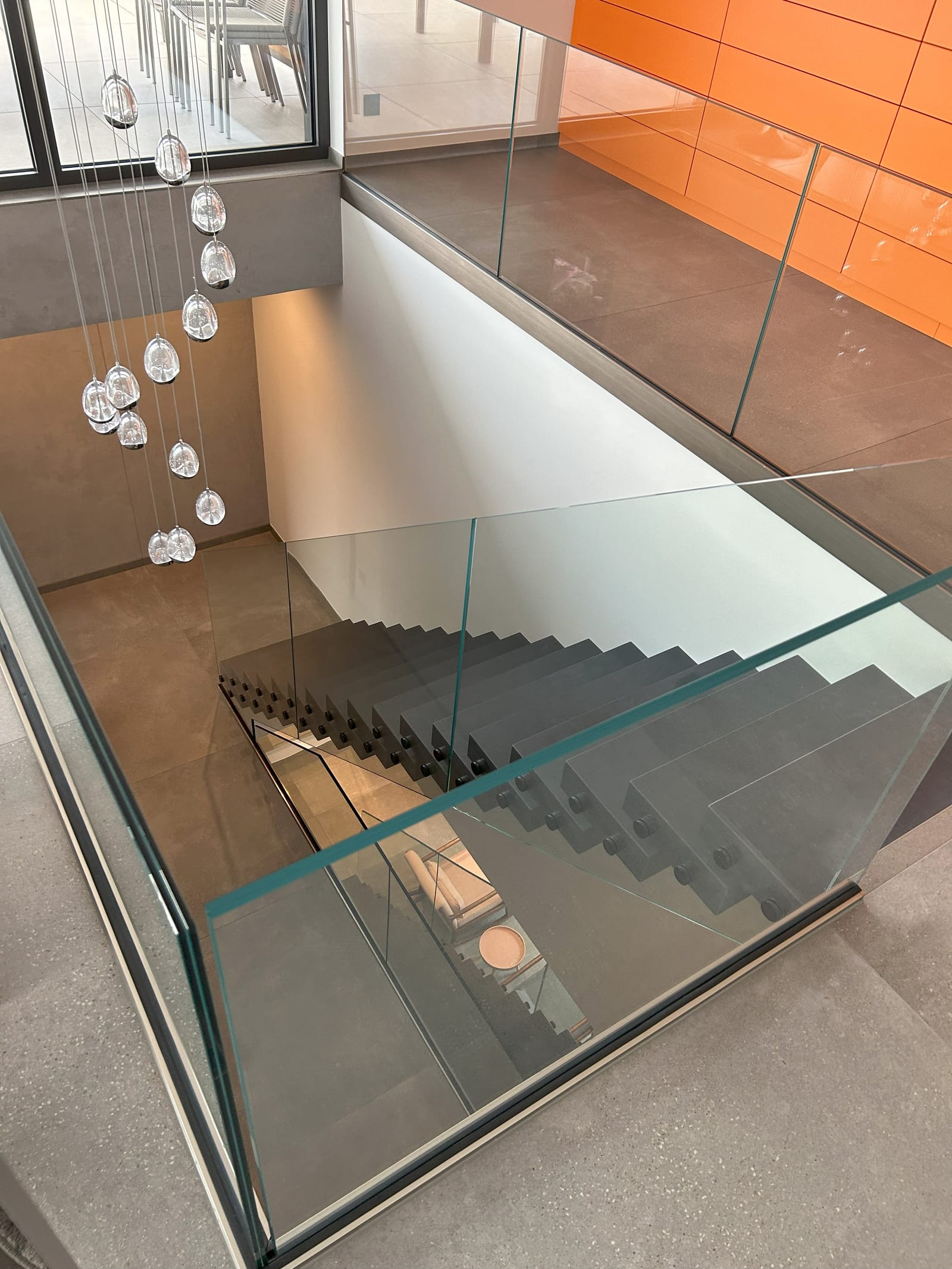 Blick von oben über die Glasbrüstung auf den dunkelgrauen Treppenlauf mit seitlichen Punkthaltern – AN Treppenbau