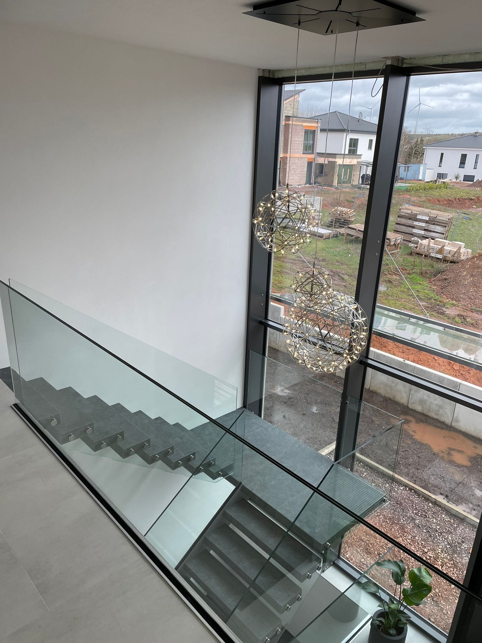 Blick von oben über das Glasgeländer auf graue Treppenstufen, daneben raumhohe Fensterfront – AN Treppenbau