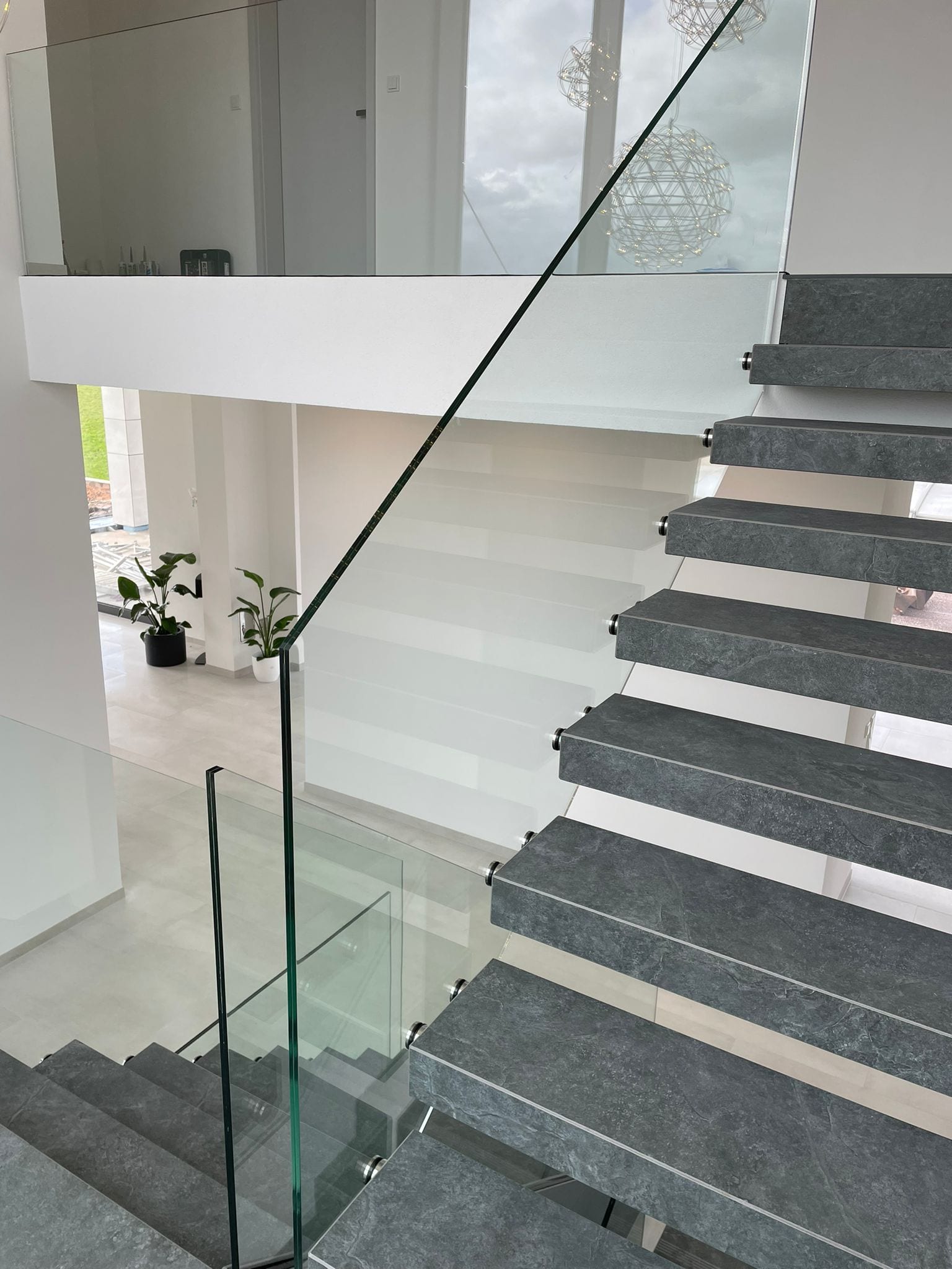 Blick von oben auf graue Stufen in Steinoptik mit Edelstahl-Punkthaltern des Glasgeländers – AN Treppenbau