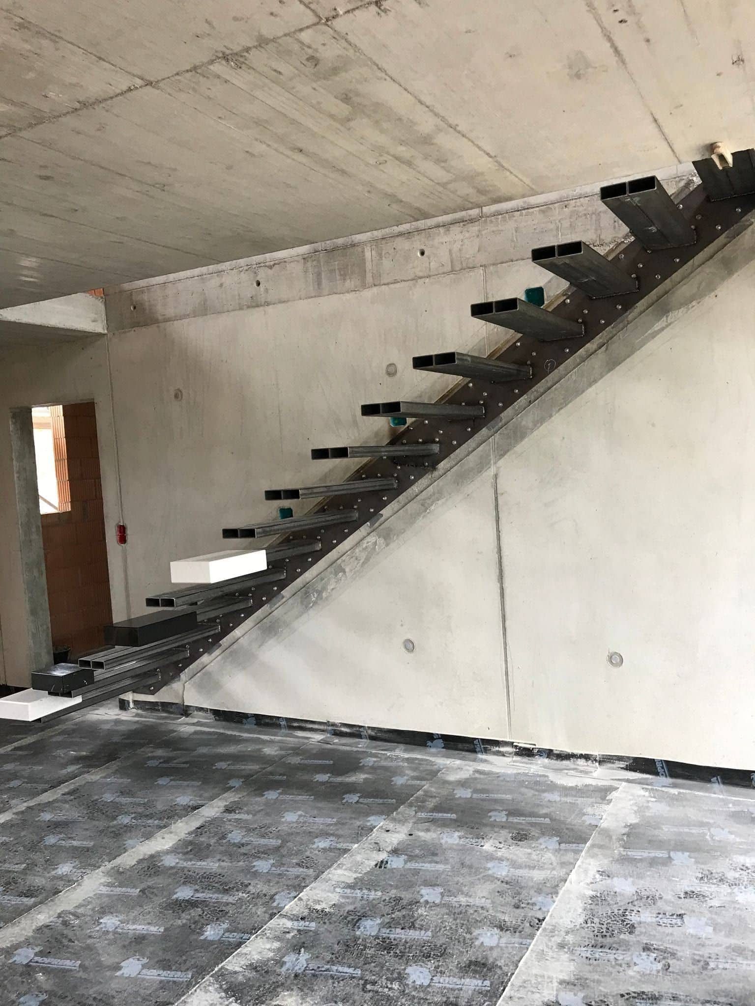 Stahlunterkonstruktion einer geraden Kragarmtreppe an einer Sichtbetonwand – AN Treppenbau