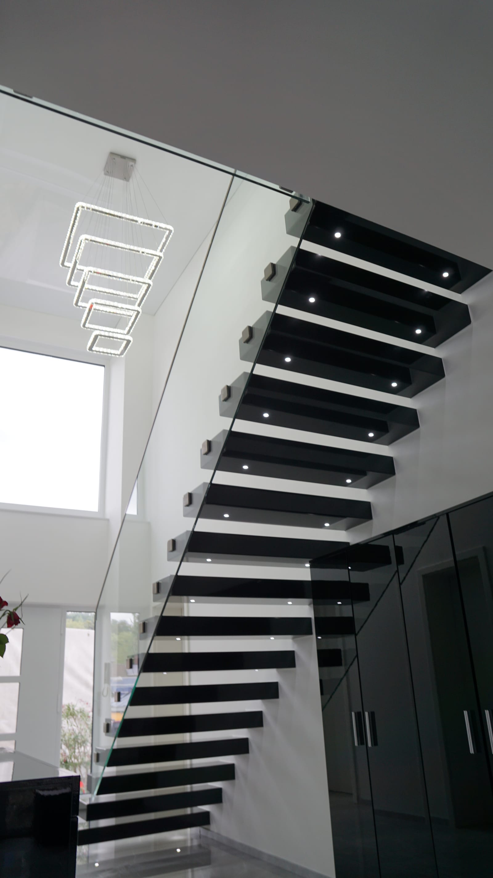 Untersicht einer Kragarmtreppe mit schwarz glänzenden Stufen, LED-Spots und Ganzglasgeländer – AN Treppenbau