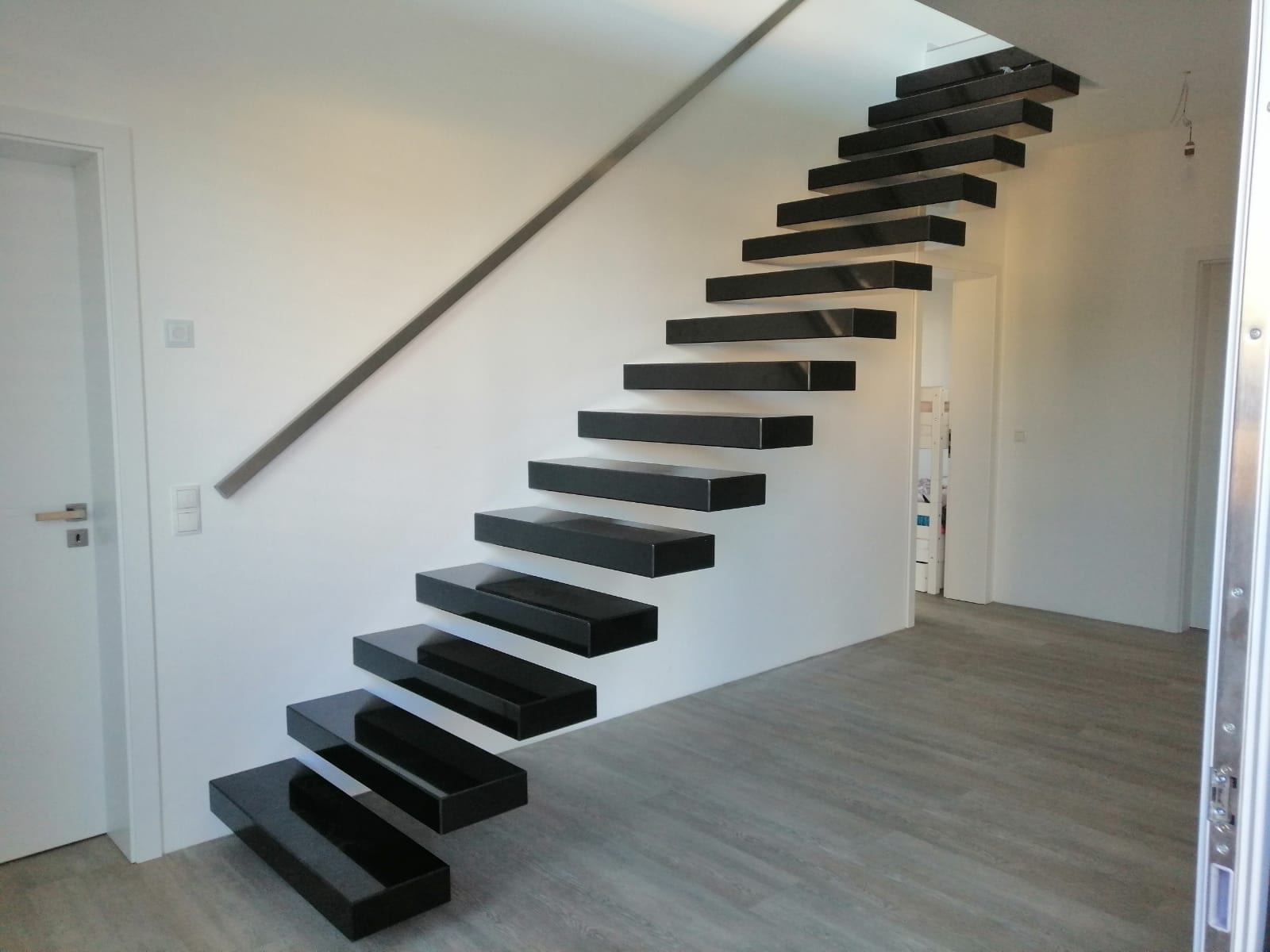 Kragarmtreppe mit schwarzen Steinstufen und Wandhandlauf, untere Stufen ragen frei in den Raum – AN Treppenbau