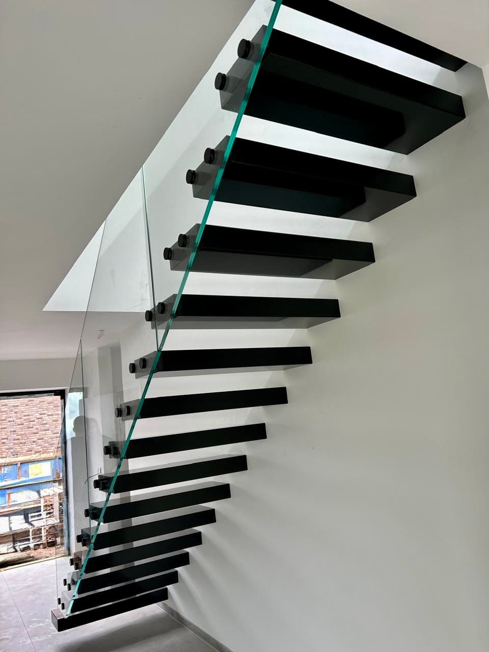 Kragarmtreppe mit dicken schwarzen Stufen und Ganzglasgeländer, von schräg unten fotografiert – AN Treppenbau
