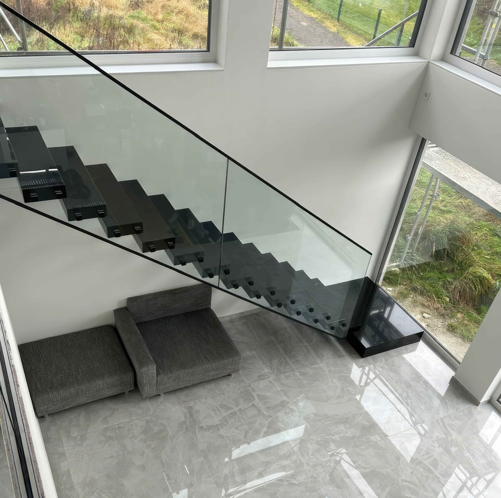 Blick von oben durch das Glasgeländer auf die dunklen, glänzenden Stufen einer Kragarmtreppe – AN Treppenbau