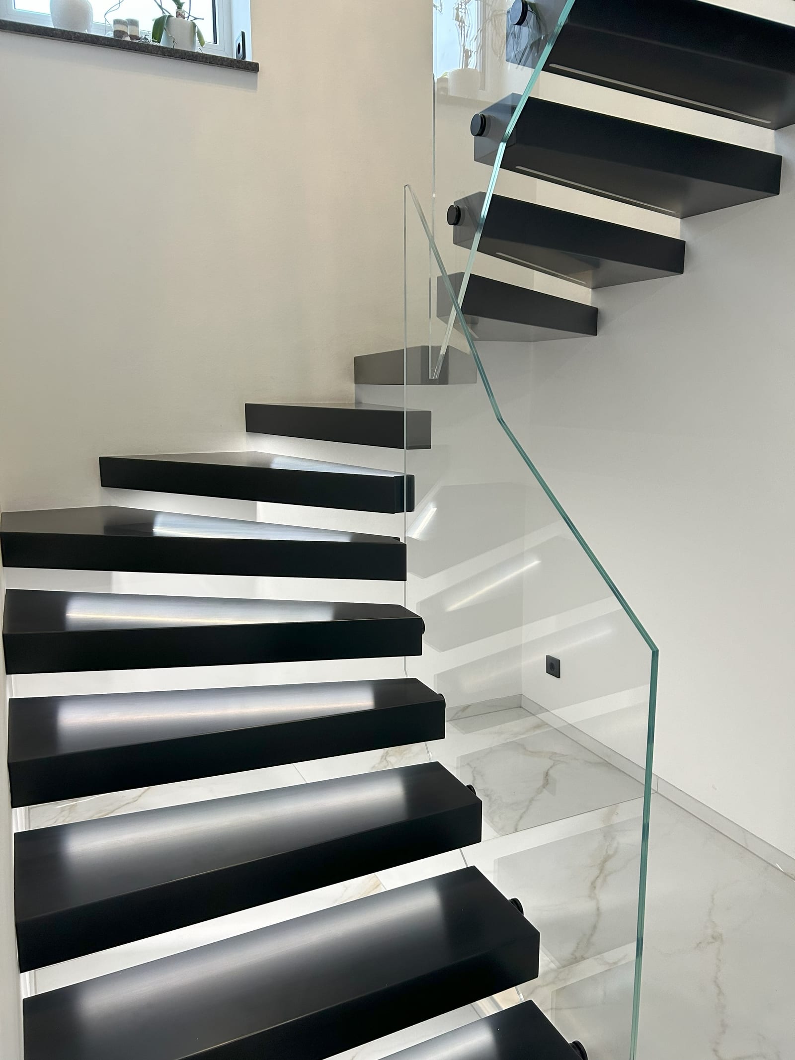 Kragarmtreppe mit schwarzen Stufen und punktgehaltenem Glasgeländer, Blick von unten den Lauf hinauf – AN Treppenbau