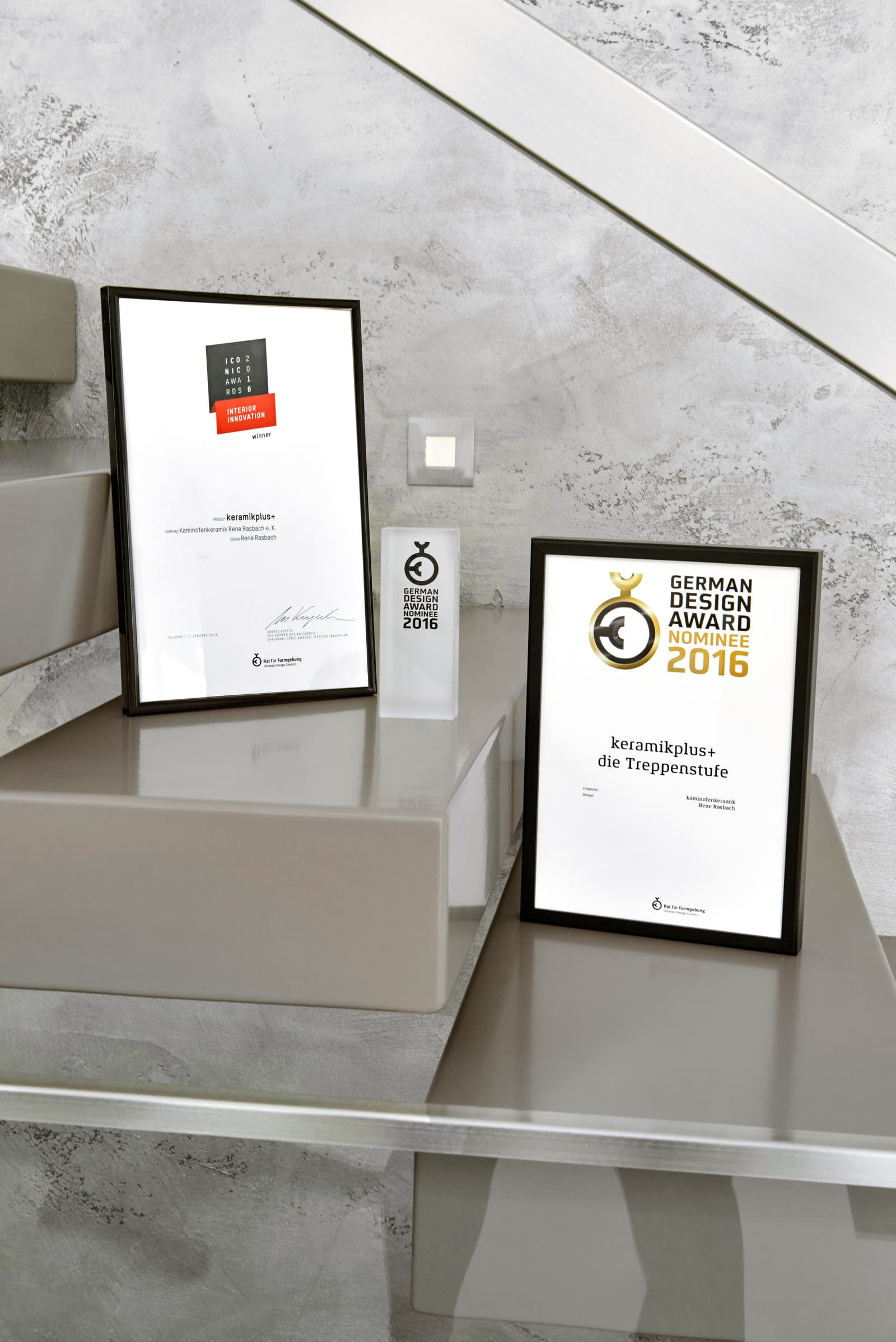 Urkunde und Trophäe des German Design Award 2016 für die Keramikstufe auf einer Kragarmstufe vor Betonoptik-Wand