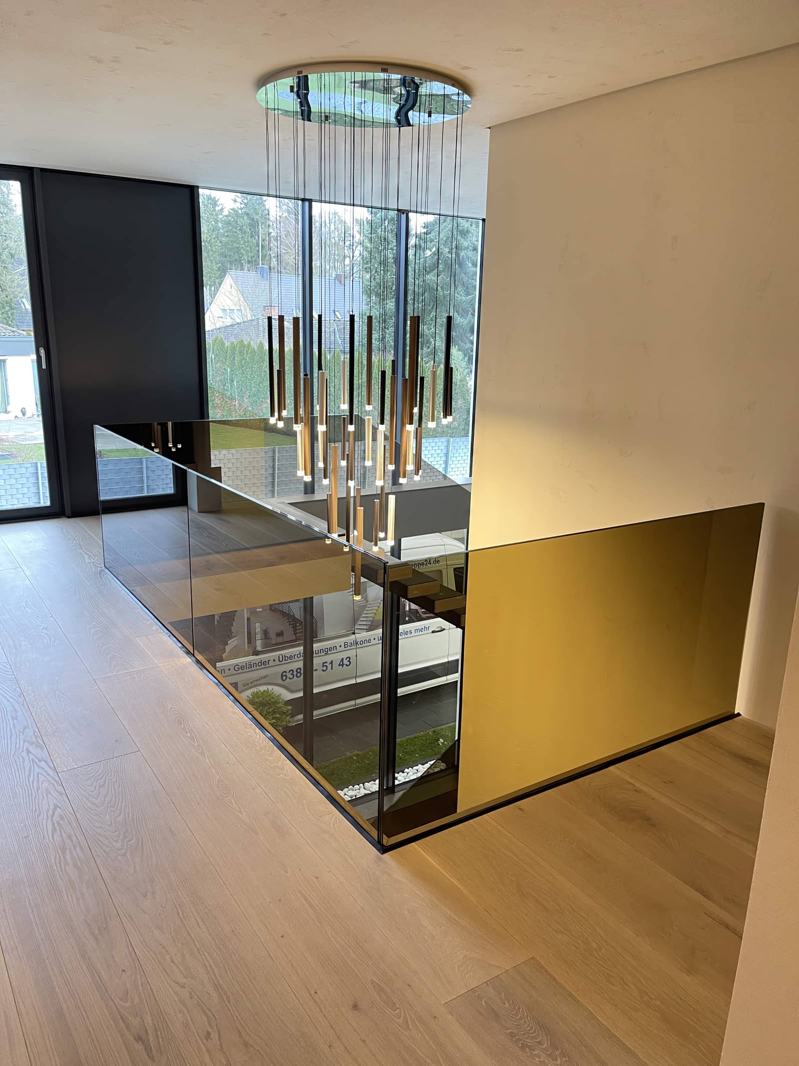 Galeriegeländer aus getöntem Glas mit Pendelleuchten über dem Luftraum, Kragarmtreppe im Hintergrund
