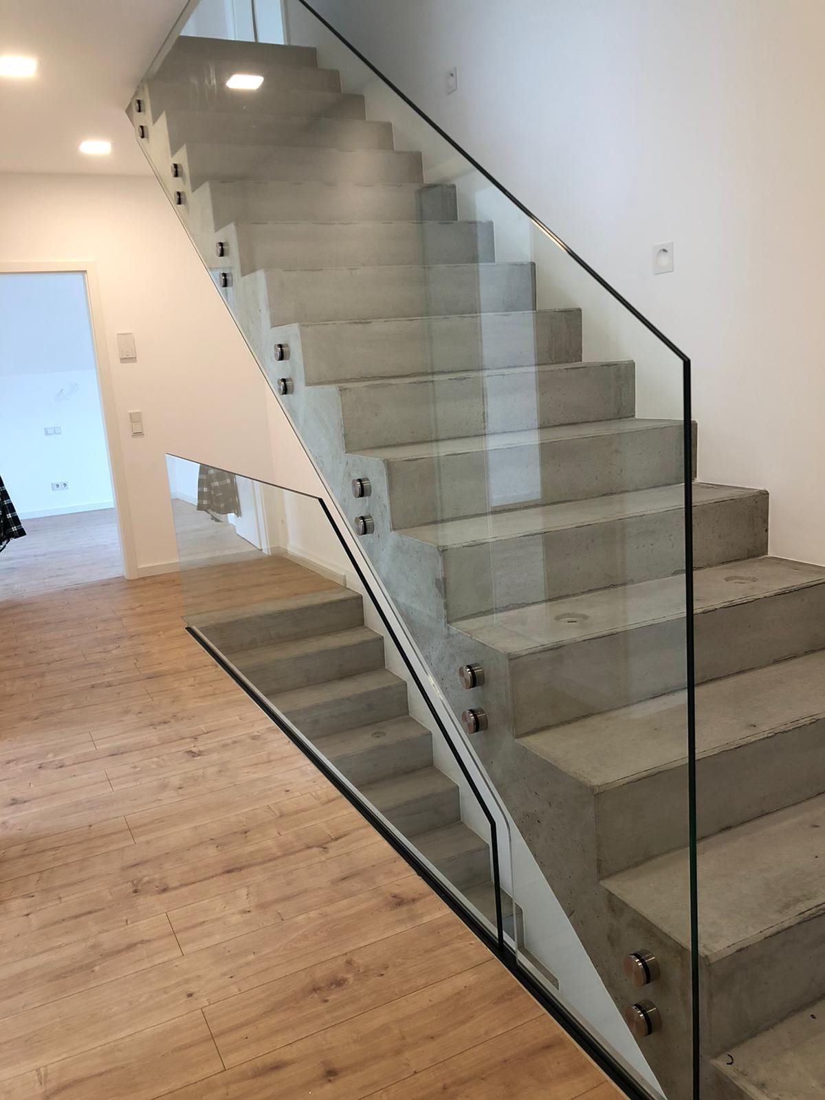 Kragarmtreppe mit Betonstufen und rahmenlosem Glasgeländer in einer Diele, Blick von unten