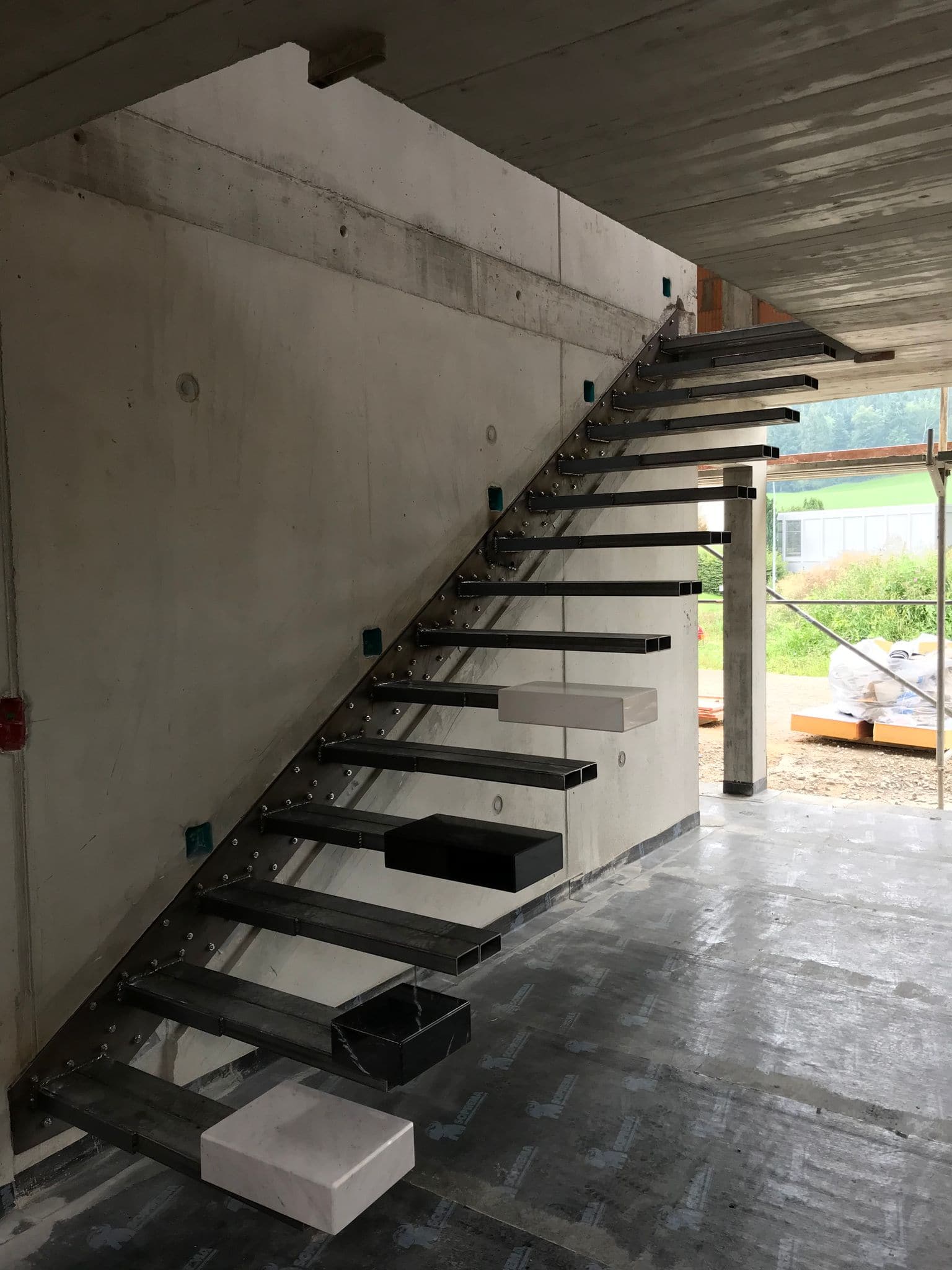 Stahl-Unterkonstruktion einer Kragarmtreppe im Rohbau an einer Betonwand, Stufenträger und Ankerplatten sichtbar