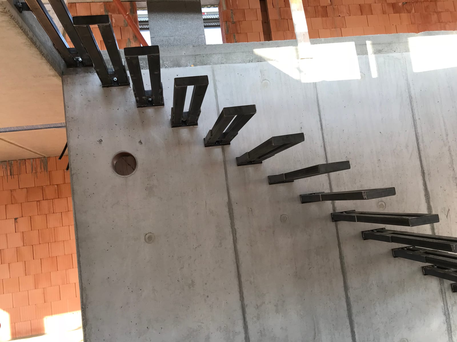 Stahlkragarme in einer Sichtbetonwand im Rohbau, daneben rotes Ziegelmauerwerk – AN Treppenbau