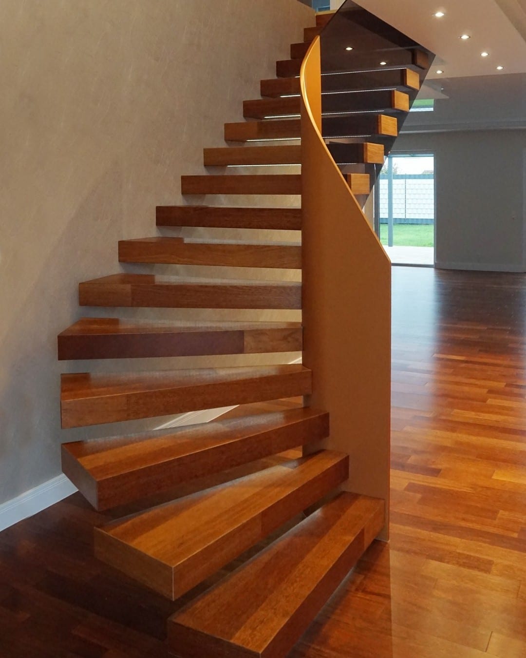 Gewendelte Kragarmtreppe aus dunklem Holz mit geschwungener Wange in einem Wohnraum mit Parkett