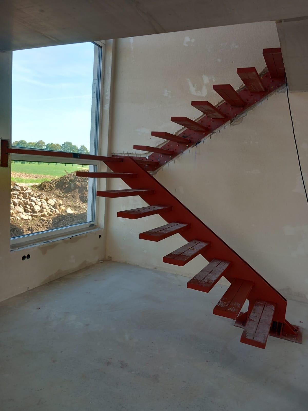 Rot grundierte Stahlkonsolen einer gewendelten Kragarmtreppe im Rohbau vor einem Fenster
