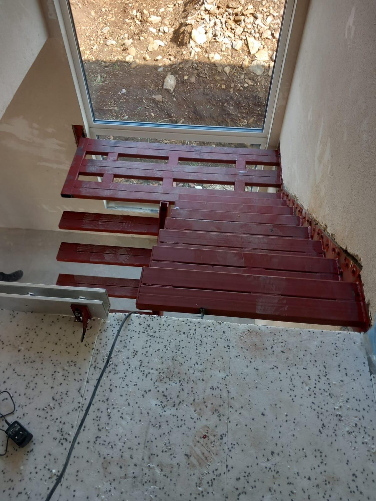 Podest und Stufenträger einer Kragarmtreppe in roter Grundierung vor dem Fenster im Rohbau