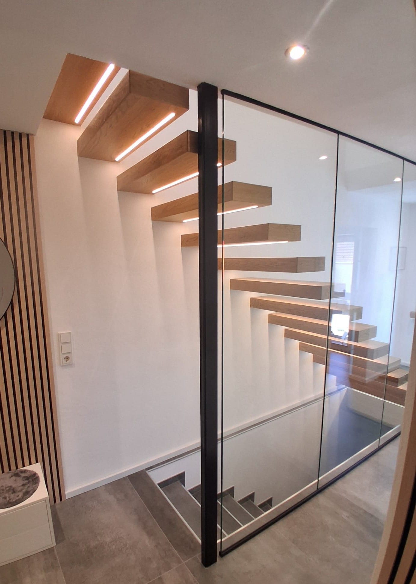 Kragarmtreppe in heller Eiche mit Glaswand und schwarzem Handlauf – AN Treppenbau