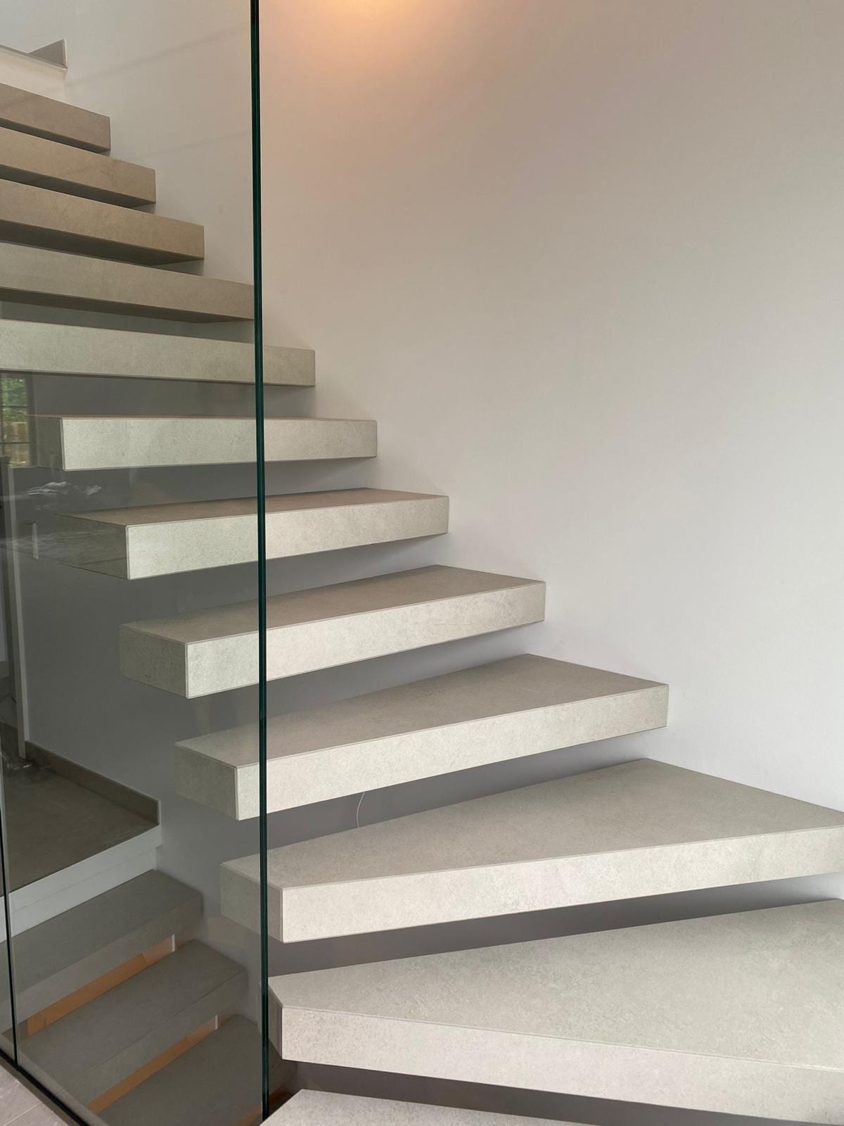 Kragarmtreppe mit hellen Steinstufen und Ganzglasgeländer – AN Treppenbau