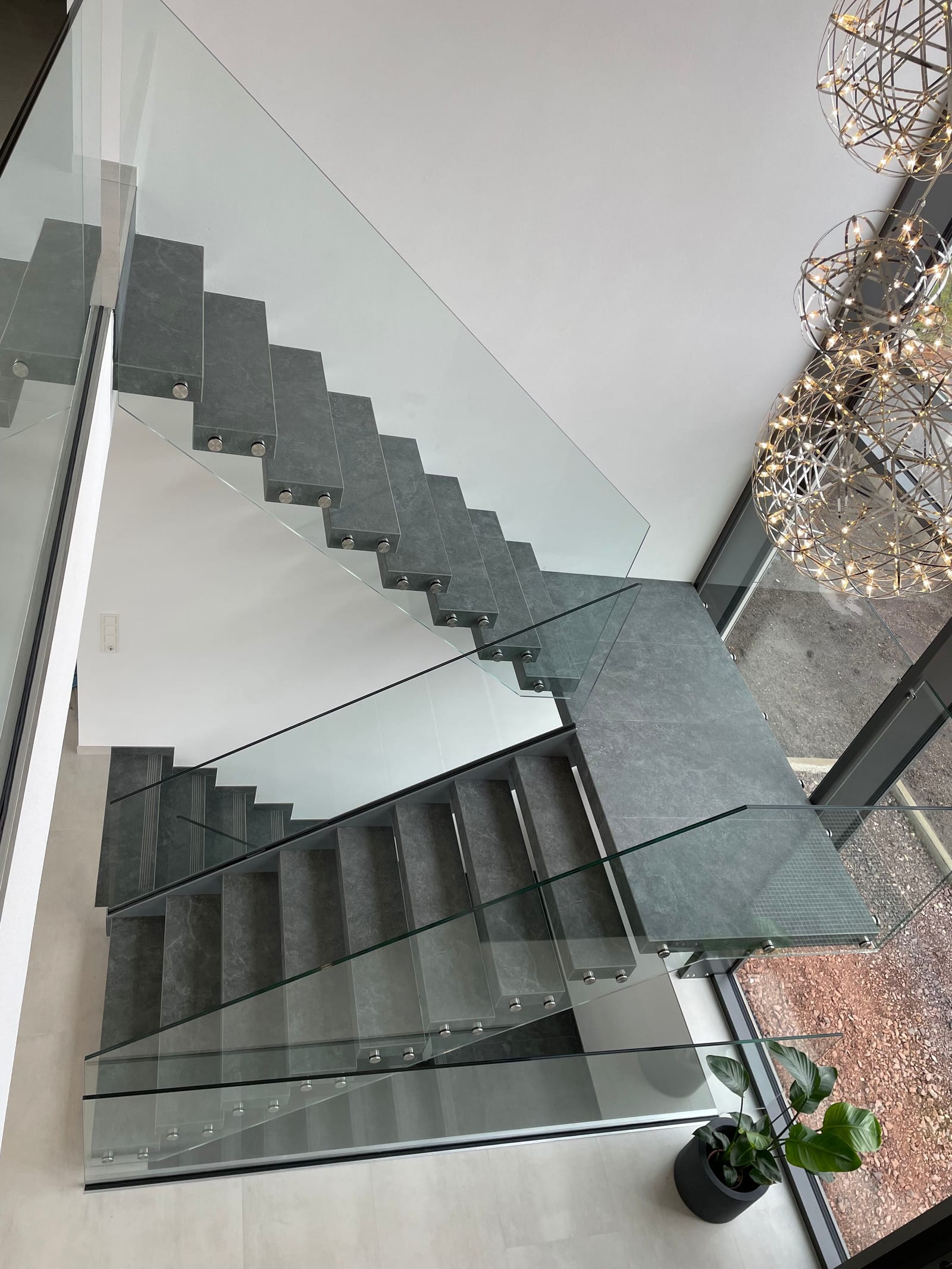Kragarmtreppe mit dunklen Steinstufen und Ganzglasgeländer, Blick von oben – AN Treppenbau